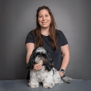 A woman smiling and holding a black and white Shih Tzu, both posing in front of a grey background.